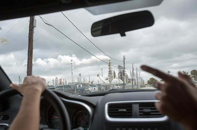 Photo of a polluting oil refinery through the windshield of a car leading a