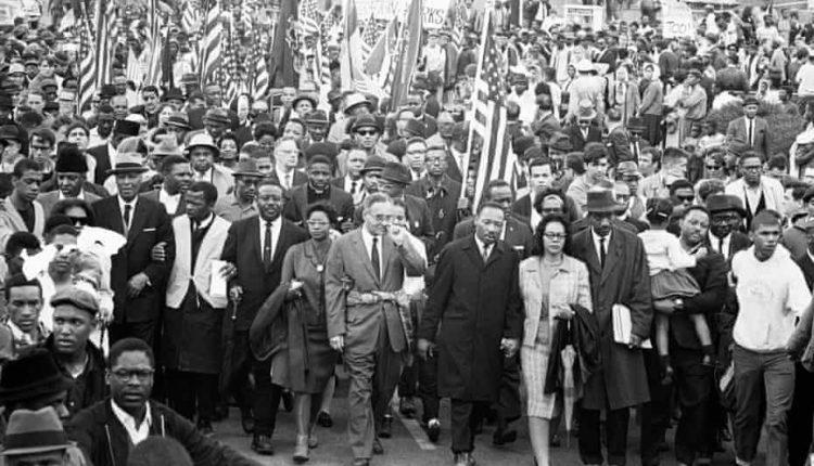 John Lewis (second from left in the main group, wearing white tunic), Dr.  Martin Luther King (center) and other civil rights activists arrive in Montgomery, Alabama, after marching from Selma in non-violent protest on March 25, 1965
