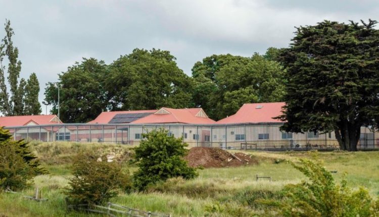 A collection of small buildings with red roofs behind a wire fence