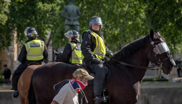 Police on horseback with helmets as a masked passerby in army cap passes by