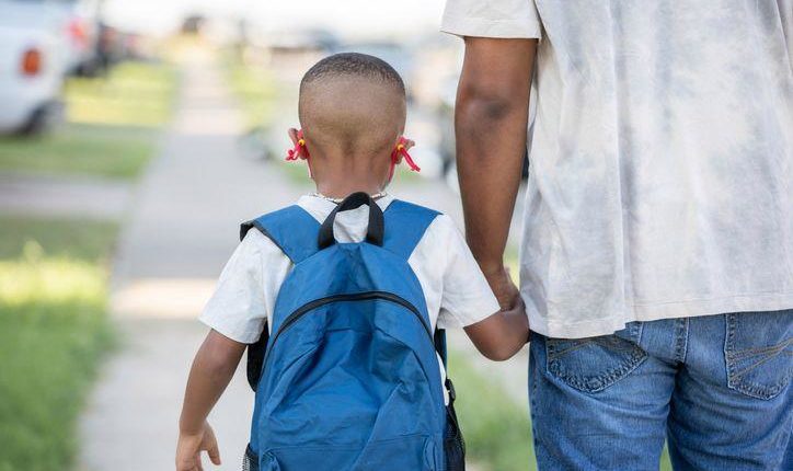 Father holds his elementary school age sons by the hand while he goes to school